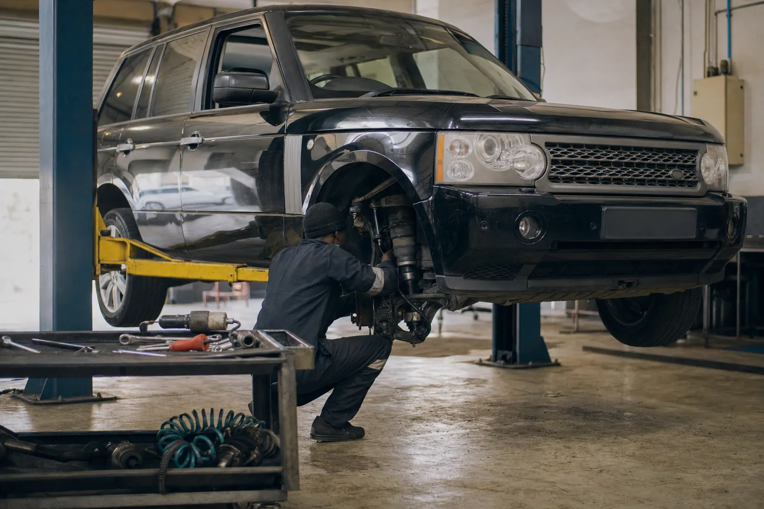 Land Rover Range Rover L322 raised on a workshop lift while a mechanic inspects the front air suspension strut