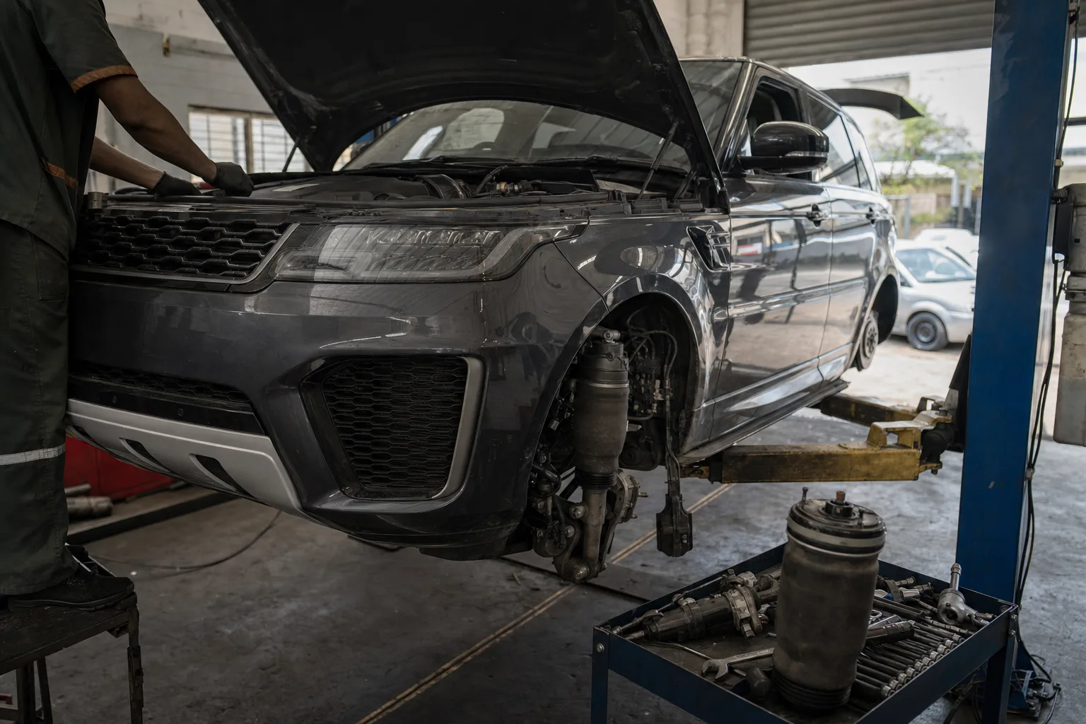 Second-generation Range Rover Sport (L494) raised on a workshop lift while a mechanic inspects the front air suspension and SDV6 engine bay